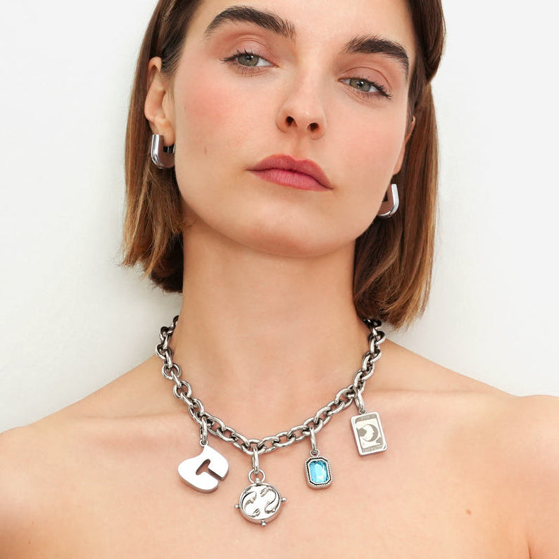 Woman wearing a silver necklace with charms on a plain background